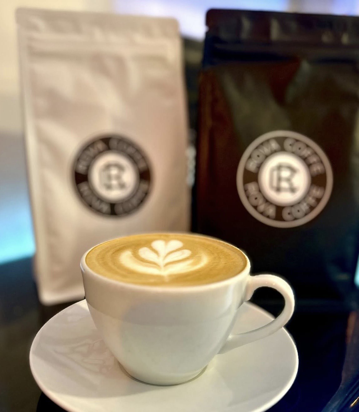 Šálek cappuccina s latte art před balením čerstvě pražené kávy Rova Coffe z české pražírny kávy